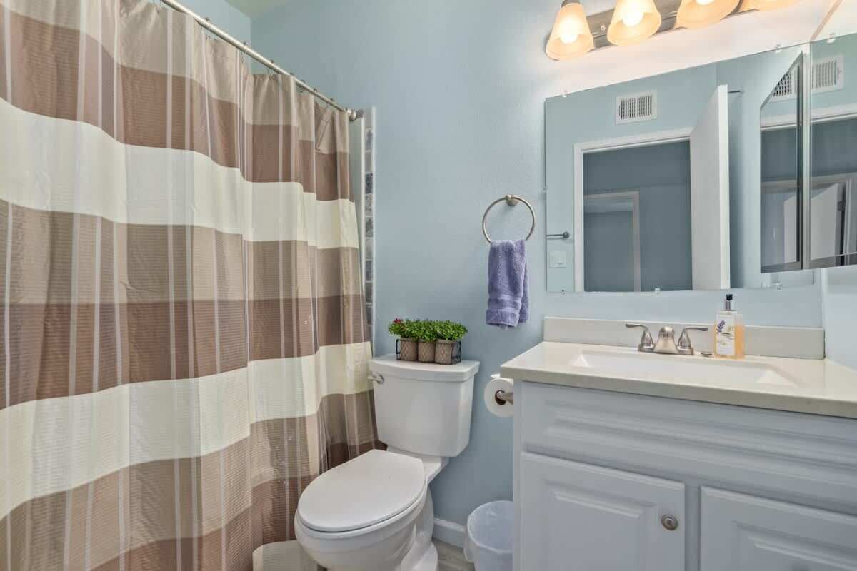 A bathroom with a striped shower curtain, a toilet, a sink with a mirror, and a towel rack with a purple towel.
