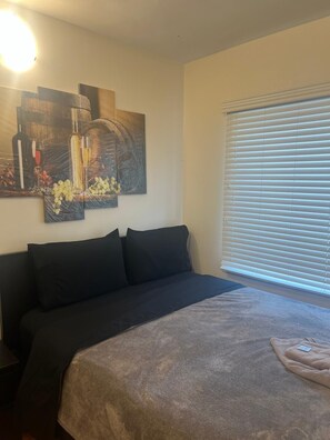 Ein Schlafzimmer mit einem Bett, einem Wandbild und einem Fenster mit Jalousien.