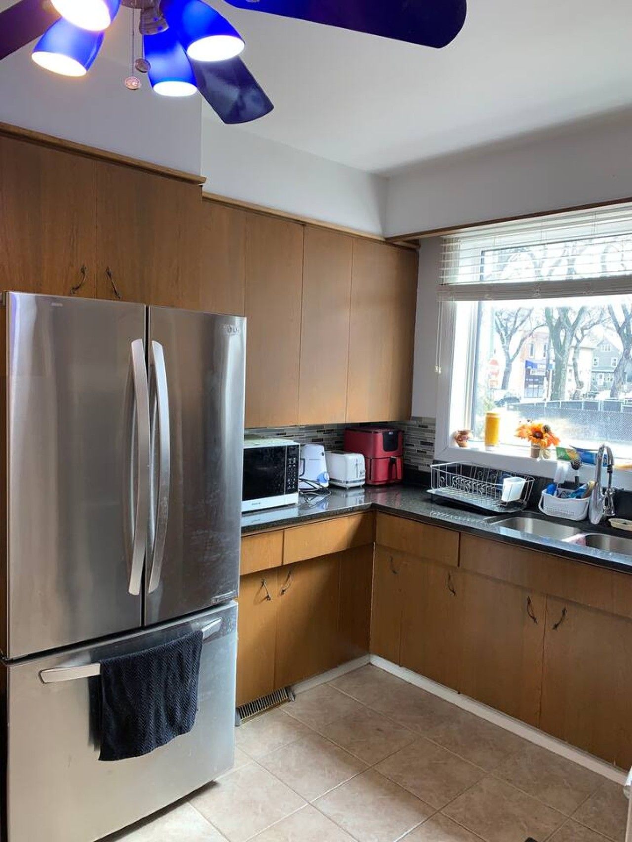 A modern kitchen with stainless steel appliances, wooden cabinets, a window with a view, and a dish rack on the countertop.