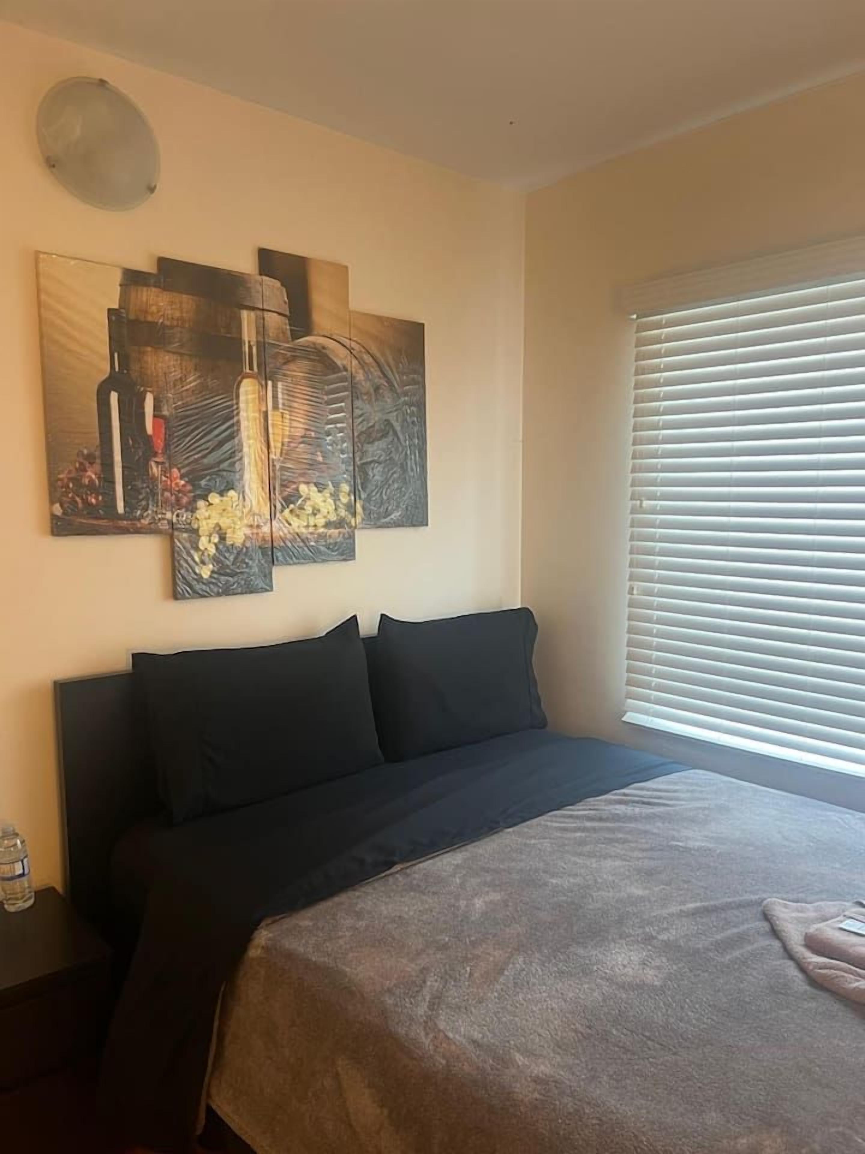 A bedroom with a bed, a wall-mounted artwork, and a window with blinds.