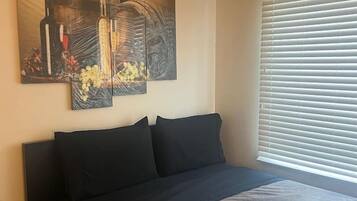 A bedroom with a bed, a wall-mounted artwork, and a window with blinds.