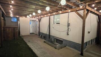 Un espace extérieur couvert, aménagé en patio, avec des poutres en bois, des guirlandes lumineuses et un sol en béton.