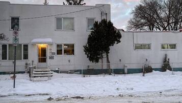 A two-story building with a snow-covered ground, a visible entrance, and a fenced yard.