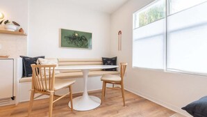 A modern living room with a white sofa, a round table, and two wooden chairs. There is a green abstract painting on the wall and a window with blinds. - Cozy Beachside Stay w/King Bed & Modern Comforts (Miami Beach)