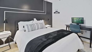 Una habitación de hotel moderna con una cama bien hecha, un escritorio con computadora y una televisión.