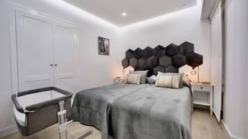 Ein modernes Schlafzimmer mit einem großen Bett, zwei Nachttischen, einer Wandleuchte und einer Tür.