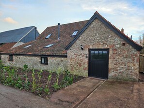 A stone building with a black door and a small garden in front.