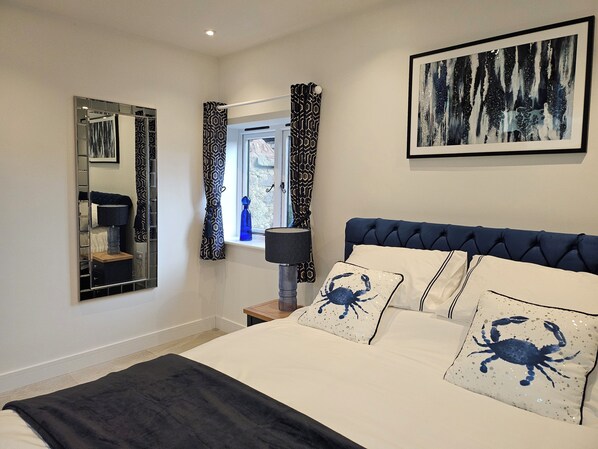 A bedroom with a bed, a nightstand, a mirror, a window with curtains, and a painting on the wall.