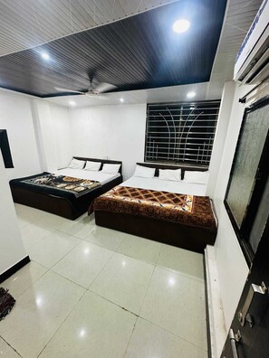 Habitación de hotel con dos camas, ventilador de techo, ventana grande con rejas y un equipo de aire acondicionado.