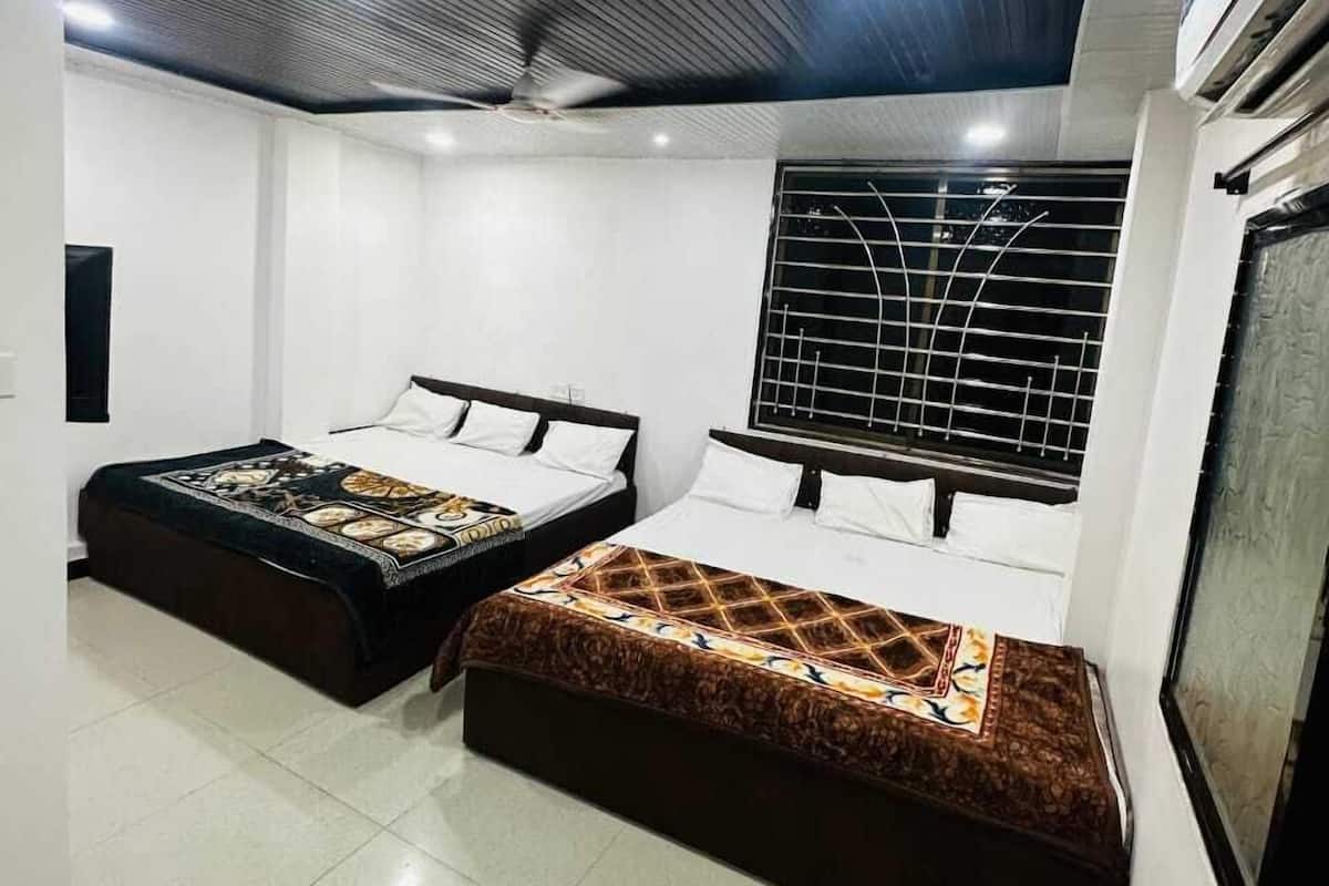 Une chambre d’hôtel moderne avec deux lits, une grande fenêtre ornée d’une grille métallique et un plafond décoré d’un motif géométrique.