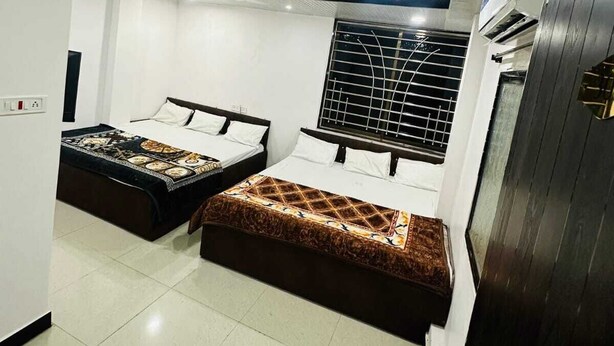 A modern bedroom with two beds, a large window with a metal grid, and an air conditioning unit. - Hotel Narmada Residency (Ujjain)