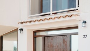 Ein Gebäude mit einer großen Holztür, einem Balkon mit Glasgeländern und einer dahinter sichtbaren Steinwand.