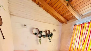 Habitación con dos camas, vigas de madera en el techo, un espejo en la pared con plantas y una cortina a rayas.