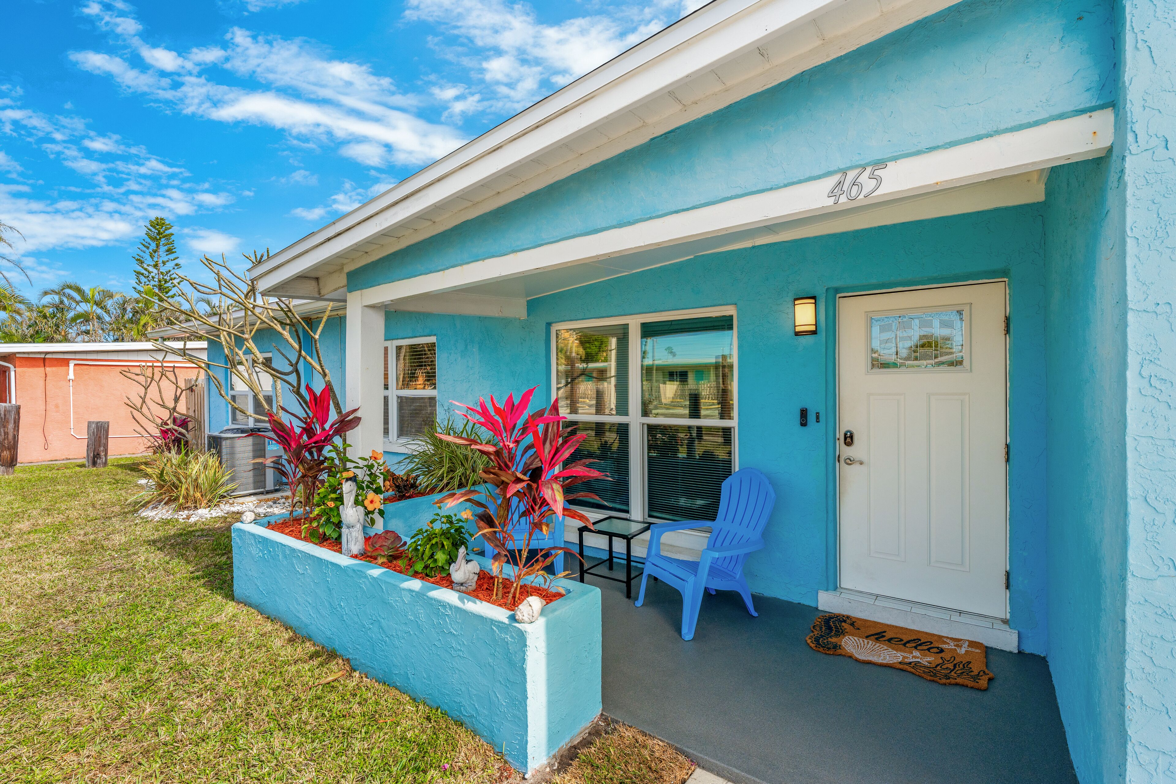 A house with a blue exterior, a white door, and a small porch with a chair and a table.