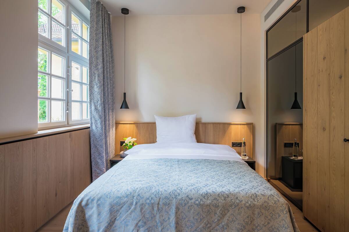Un lit bien fait, recouvert d’une couvre-lit à motifs, avec deux lampes de chevet et une table de chevet ornée d’un vase de fleurs.