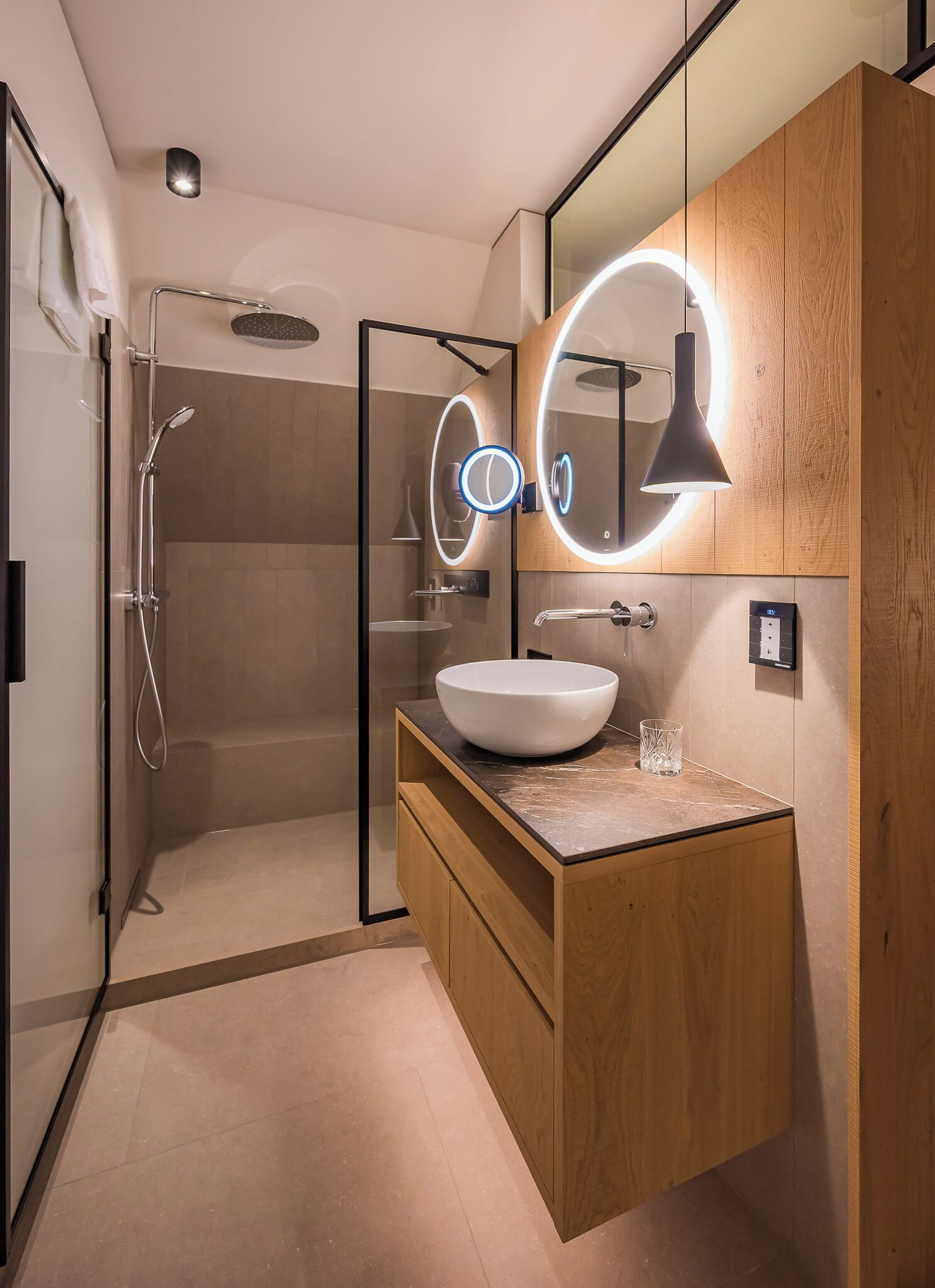 Une salle de bain moderne avec un grand miroir, un luminaire rond et un meuble-lavabo en bois.