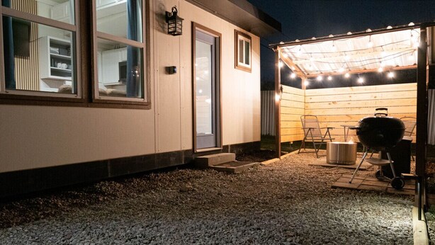 A covered outdoor patio with a barbecue grill, string lights, and a seating area. - Modern Tiny Home 15 mins from Fort Worth (Fort Worth)