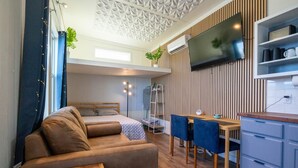 A modern, compact room with a sofa, a small dining table, a TV, and a kitchenette. - Modern Tiny Home 15 mins from Fort Worth (Fort Worth)