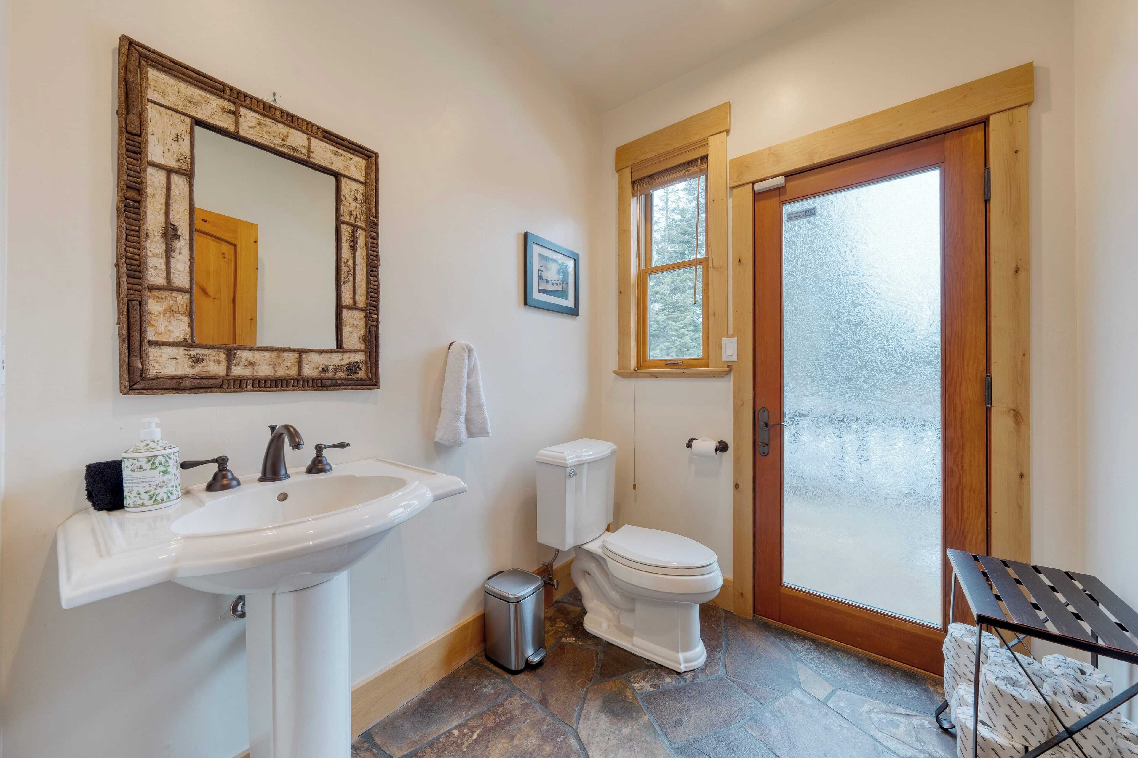 Een badkamer met een wit wastafelmeubel, een spiegel, een toilet en een deur die leidt naar een etalageraam met frosted glass.
