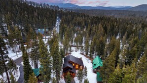 A cabin with a sloped roof surrounded by a forest, a winding road, and a mountain range in the background. - 5 Mins to Ski Resort Ping Pong, Pool Table, Deck Donner Ridge by Avantstay (Truckee)
