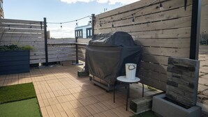 En terrasse med grill, et lille rundt bord og lyskæder.