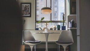 Et moderne spiseområde med et rundt bord, to stole, en hængende lampe og et vindue med udsigt over byen.