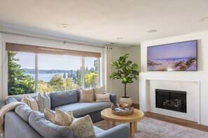 A modern living room with a large window, a fireplace, and a view of the outdoors.