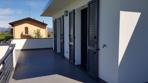 Un balcon avec un sol carrelé, une balustrade et, en arrière-plan, un bâtiment doté de volets.
