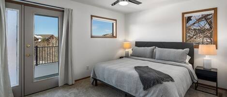 A bedroom with a bed, two bedside tables with lamps, a ceiling fan, and a view through a door.