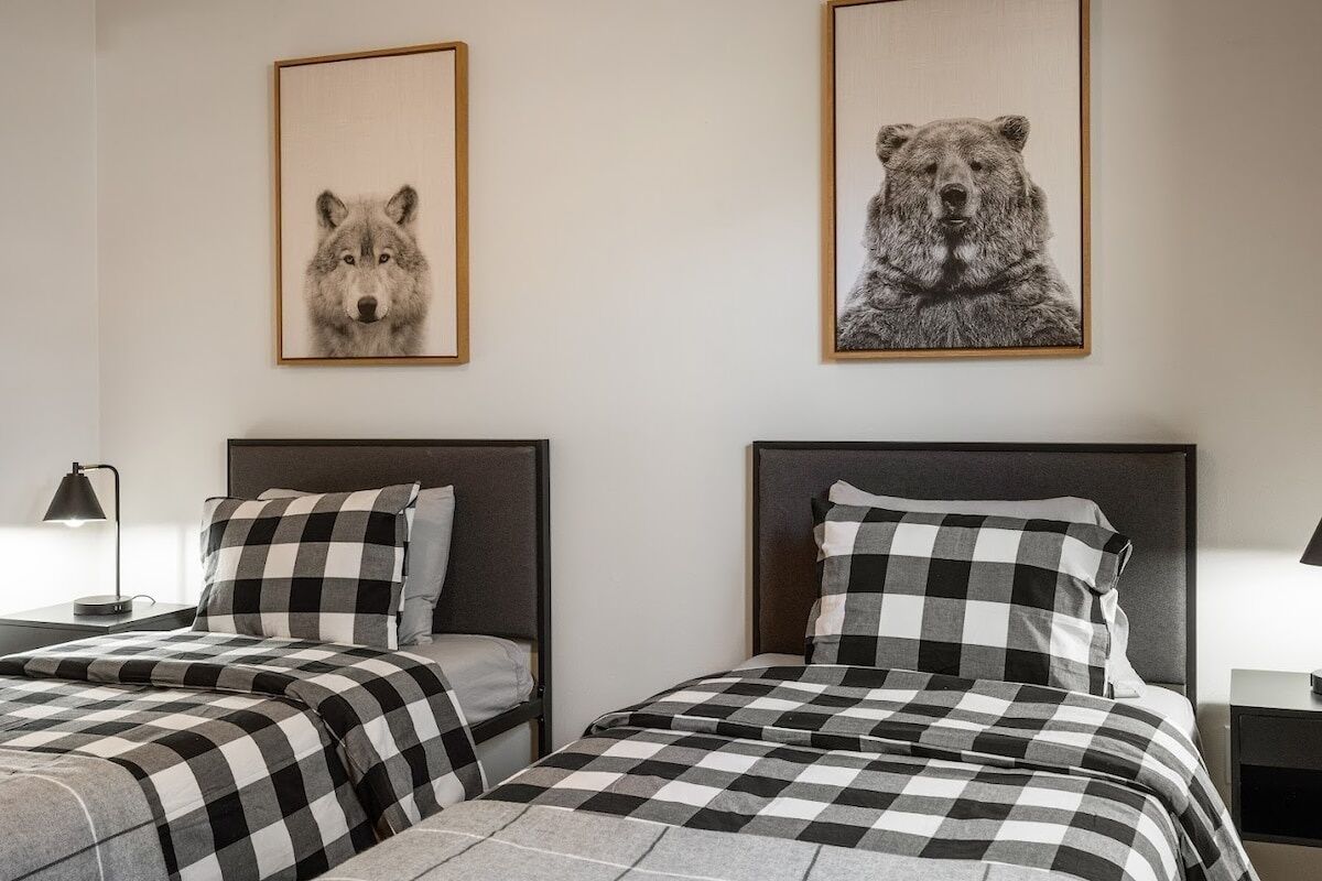 A hotel room with two beds, each with a checkered bedspread and matching pillows. There are framed animal prints on the wall above the beds.