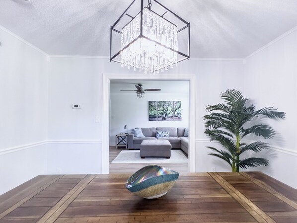 Un salon moderne avec un plancher en bois, un lustre en verre, un canapé gris et une grande plante en pot.