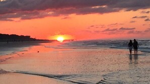 Un atardecer sobre una playa con dos personas caminando.