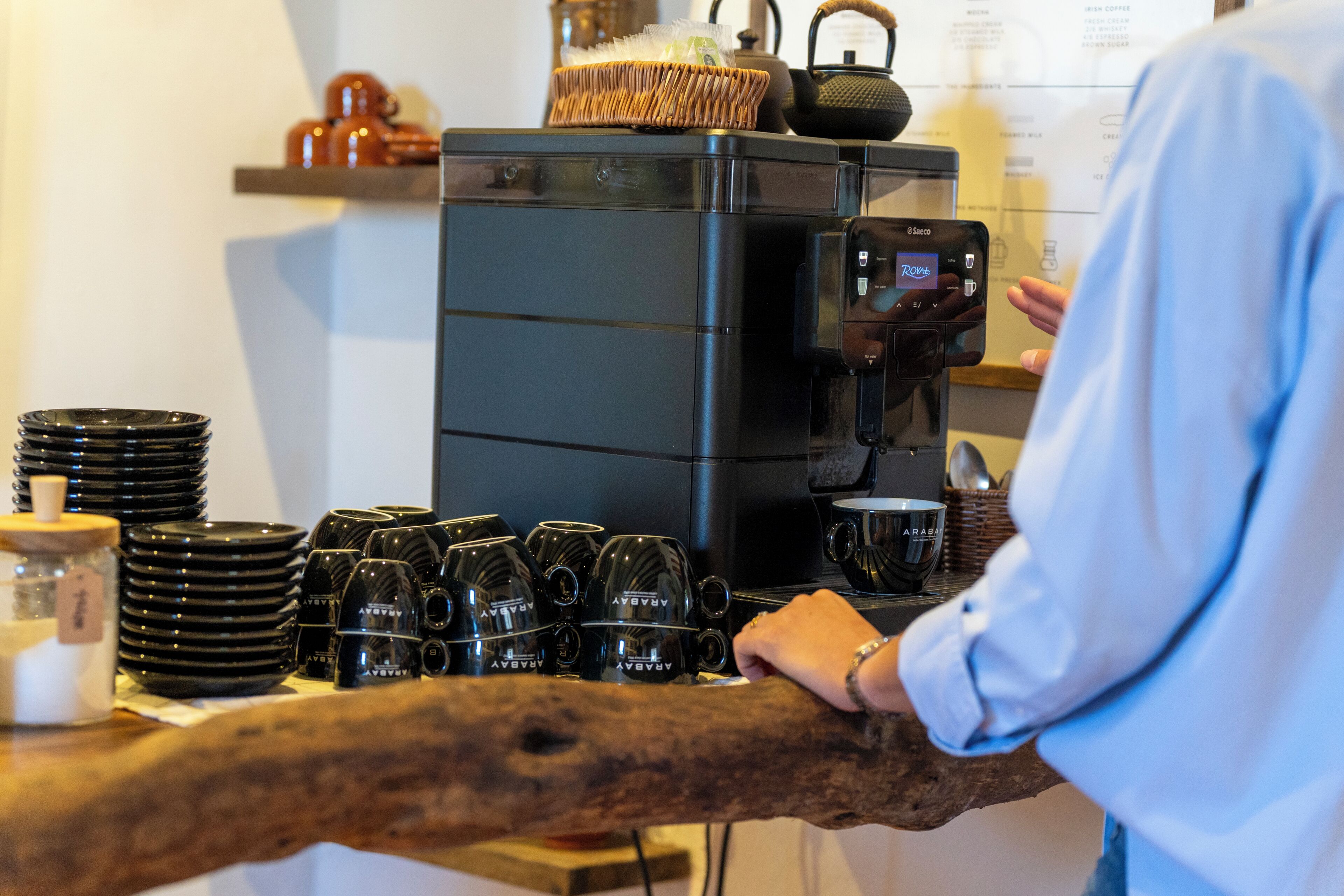 Una cafetera, tazas negras y una pila de platos sobre una encimera.