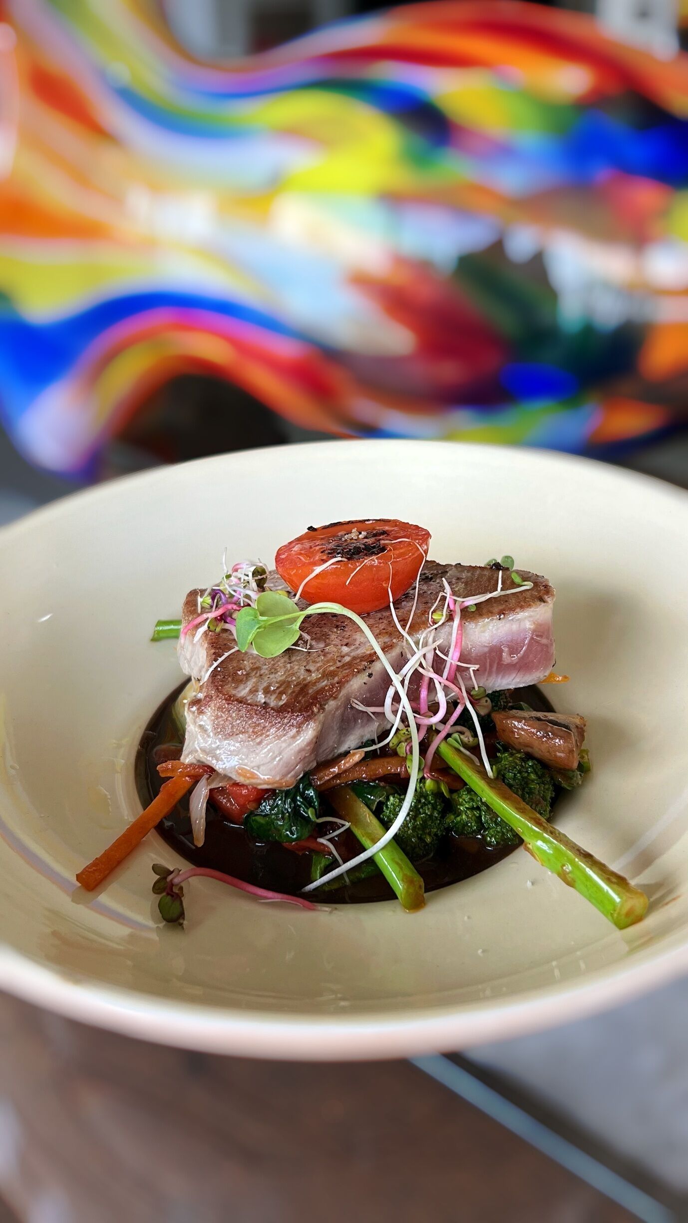 A plate of food with a piece of meat, vegetables, and a tomato.