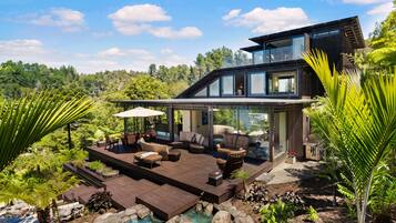 Una casa moderna de dos pisos con una amplia terraza, mobiliario exterior y una piscina.