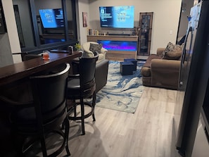 A modern living room with a bar area, a flat-screen TV, and a fireplace.