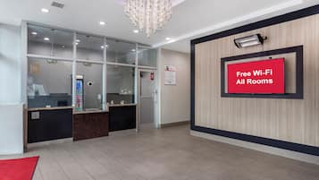 A hotel reception area with a modern design, including a reception desk, a glass partition, a chandelier, and a sign indicating free Wi-Fi availability.