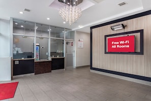 Zona de recepción de un hotel con diseño moderno, que incluye un mostrador de recepción, un panel de vidrio, una araña y un letrero que indica disponibilidad de Wi-Fi gratuito.