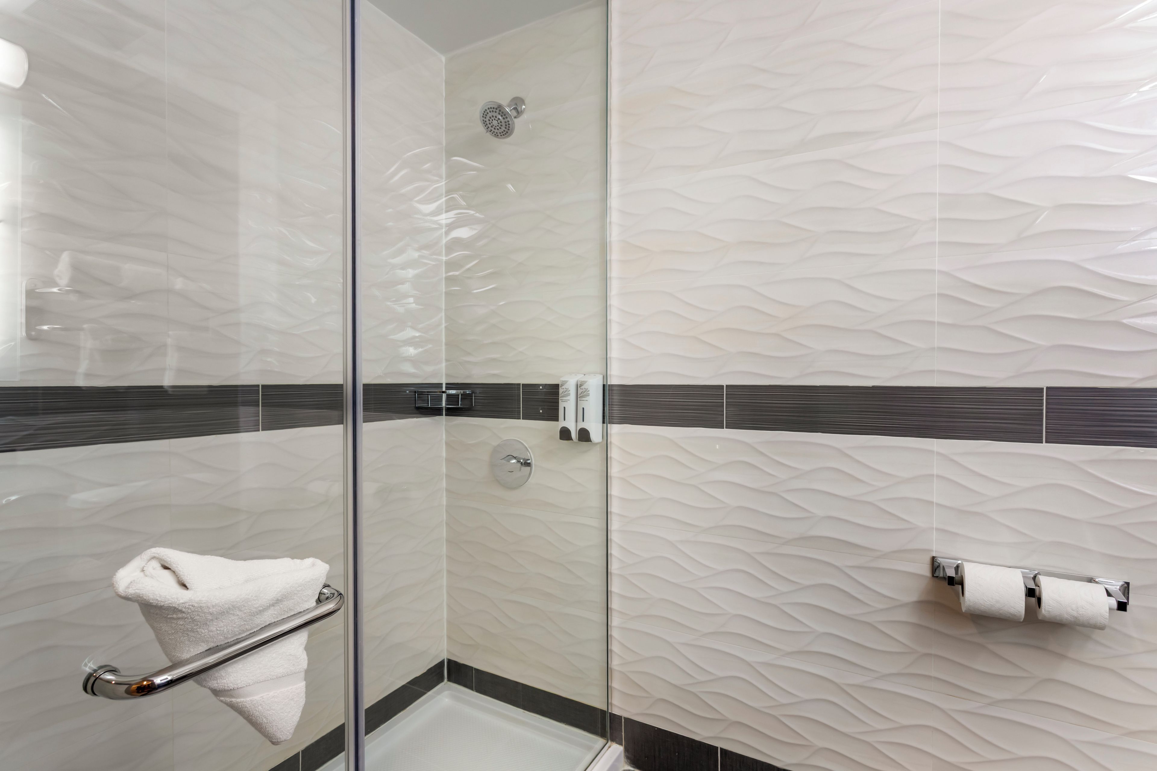 A modern bathroom with a glass shower enclosure, a towel rack, and a toilet paper holder.