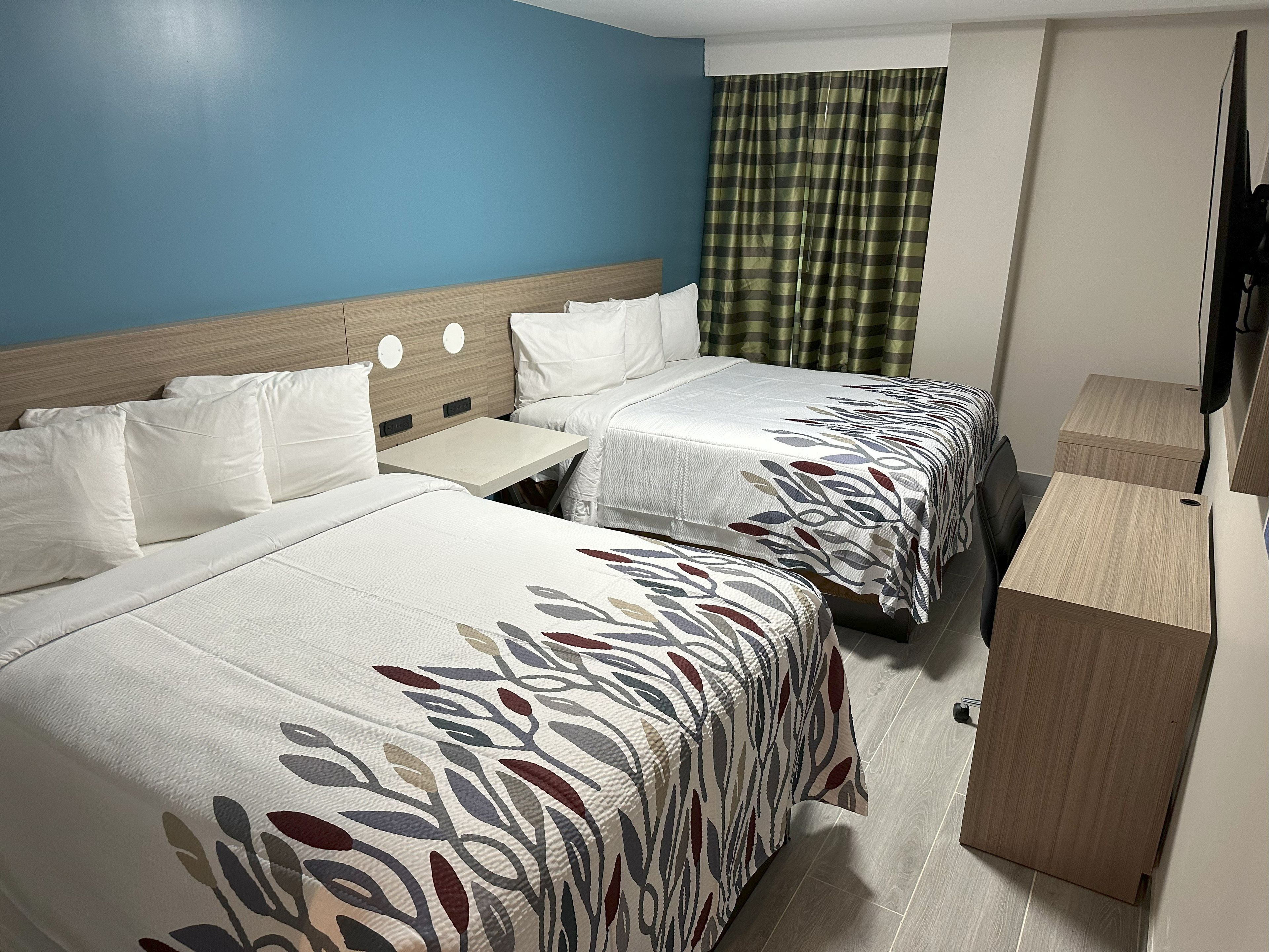 A hotel room with two beds, a small table, a wooden cabinet, and a television.