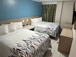 Habitación de hotel con dos camas, una mesita pequeña, un armario de madera y un televisor.