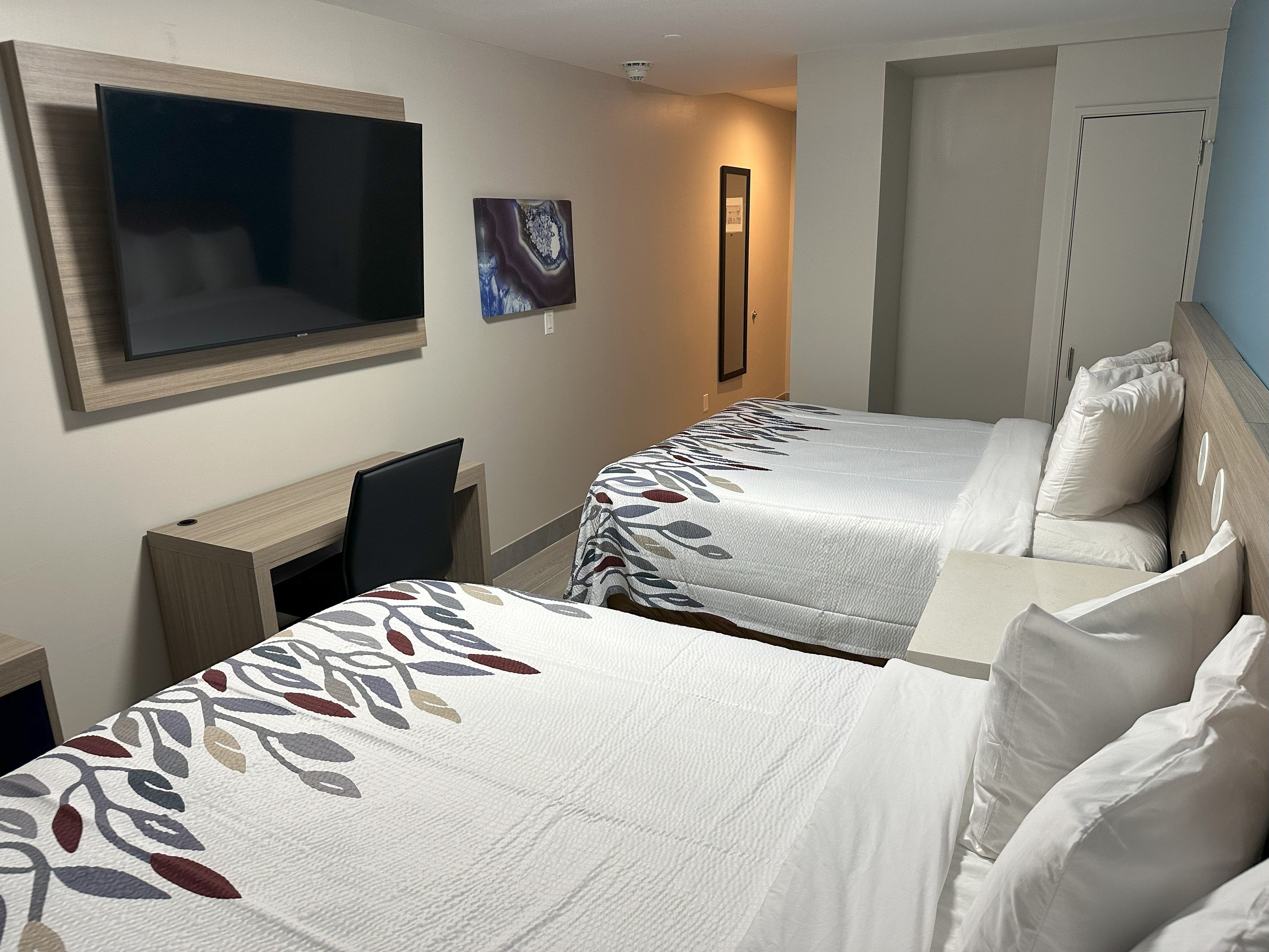 Habitación de hotel con dos camas, un televisor, un escritorio y un espejo.
