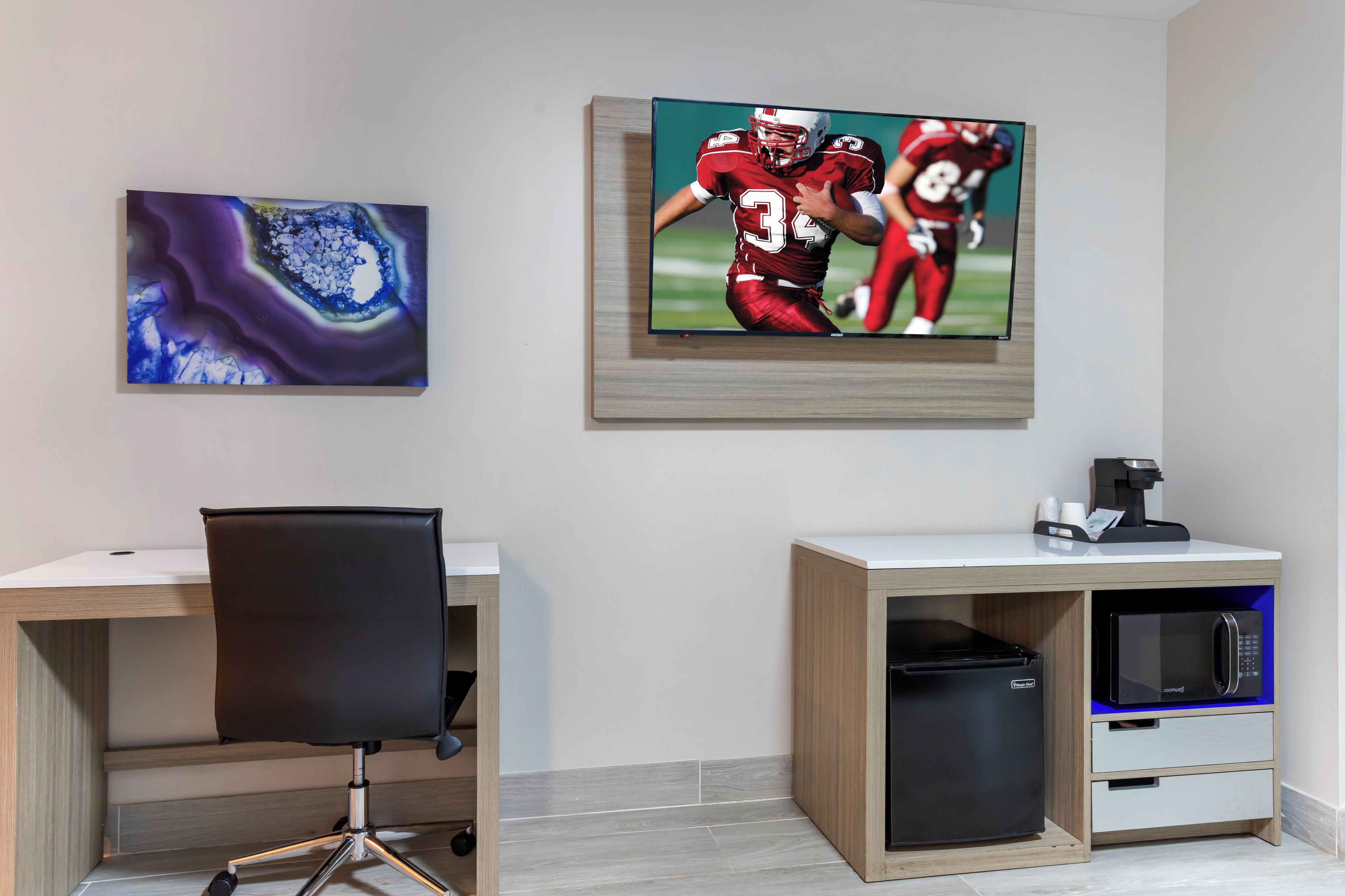 A modern office space with a desk, chair, and a television mounted on the wall displaying a sports game.