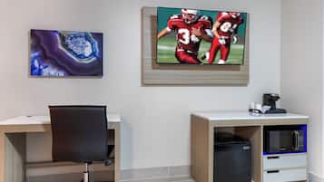 A modern office space with a desk, chair, and a television mounted on the wall displaying a sports game.