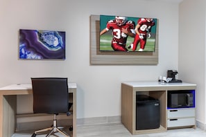 Un espacio de oficina moderno con un escritorio, una silla y un televisor en la pared mostrando un partido deportivo.