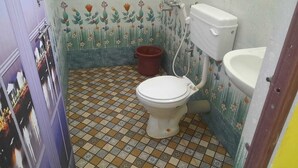 A small bathroom with a toilet, bidet, and sink. The floor has a patterned tile design. - Green tune  (Gokarna)