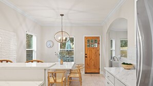 A modern kitchen with a marble countertop, wooden chairs, a wooden door, and a stainless steel refrigerator.
