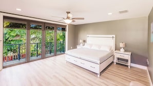 Une chambre dotée d’un grand lit, d’un ventilateur de plafond, d’une table de chevet et offrant une vue sur la verdure grâce à de grandes fenêtres.