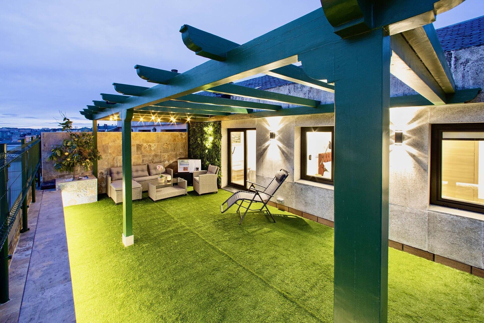 En täckt uteplats med konstgräs, utemöbler och en pergola.