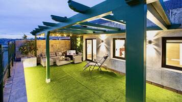 En täckt uteplats med konstgräs, utemöbler och en pergola.